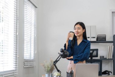 Güzel Asyalı iş kadını, kahve içiyor, bilgisayarla ofiste çalışıyor...