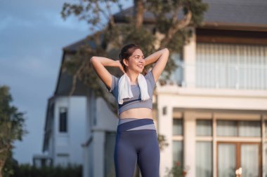 Genç Asyalı bir kadın evinin önündeki parkta spor yapmadan önce egzersiz yapıyor. Dışarıda ısınan sağlıklı bir kadın vardı. Kollarını uzatıyordu ve başka tarafa bakıyordu...