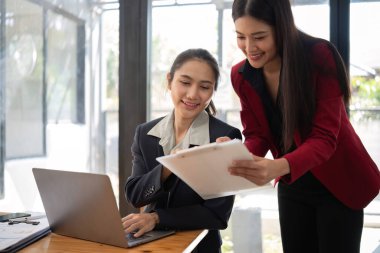 Ofis konferans odasında proje stratejisini tartışan iki iş kadını, modern işyerindeki iş arkadaşlarıyla proje planlamasını tartışıyor, mali veri raporu hakkında tavsiyelerde bulunuyor.