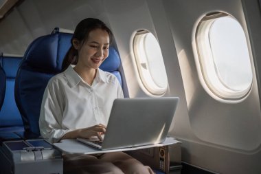 Başarılı ve profesyonel bir Asyalı iş kadını, gideceği yere uçuş sırasında bilgi toplamak için dizüstü bilgisayar kullanır...