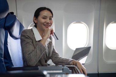 Uçaktaki çekici Asyalı kadın yolcu dizüstü bilgisayar ve kredi kartı kullanarak rahat koltukta oturuyor, kablosuz bağlantıyı kullanarak alışveriş yapıyor, tarz olarak seyahat ediyor..