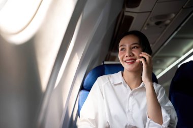 Bir uçak kabininde otururken rahat bir uçuşun keyfini çıkaran gülümseyen Asyalı kadın uçakta kablosuz internet var. Pencerenin yanındaki yolcular.