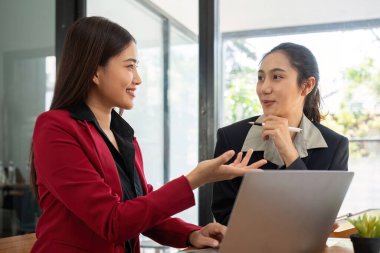 Ofis konferans odasında proje stratejisini tartışan iki iş kadını, modern işyerindeki iş arkadaşlarıyla proje planlamasını tartışıyor, mali veri raporu hakkında tavsiyelerde bulunuyor.