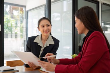 Ofis konferans odasında proje stratejisini tartışan iki iş kadını, modern işyerindeki iş arkadaşlarıyla proje planlamasını tartışıyor, mali veri raporu hakkında tavsiyelerde bulunuyor.