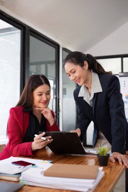 Ofis konferans odasında proje stratejisini tartışan iki iş kadını, modern işyerindeki iş arkadaşlarıyla proje planlamasını tartışıyor, mali veri raporu hakkında tavsiyelerde bulunuyor.