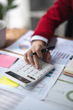İş kadını ya da muhasebecinin elinde bir kalem tutarak iş verilerini hesaplamak için hesap makinesi üzerinde çalışan bir kadının ellerini kapatın. Ofis işletme fikrinde muhasebe belgeleri ve dizüstü bilgisayar.