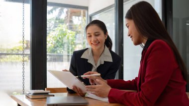 Ofis konferans odasında proje stratejisini tartışan iki iş kadını, modern işyerindeki iş arkadaşlarıyla proje planlamasını tartışıyor, mali veri raporu hakkında tavsiyelerde bulunuyor.