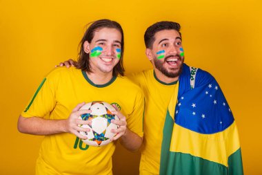 Brezilyalı arkadaşlar, Latin Amerikalılar, çeşitlilik, Brezilya için tezahürat, 2022 Dünya Kupası 'nda, topu ve bayrağı tutuyorlar, oyuna özen gösteriyorlar, mutlu, TV' de, stadyumda maç seyrediyorlar.