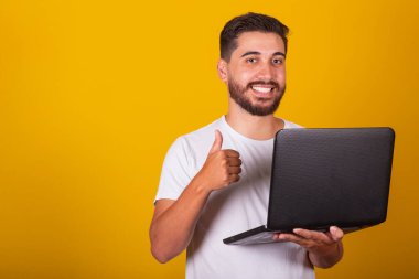 Brezilyalı Latin Amerikalı adam, mutlu, elinde not defteri ve gülümseme, başparmağıyla iş konsepti, onay, iyimserlik, teknoloji, internet erişimi.