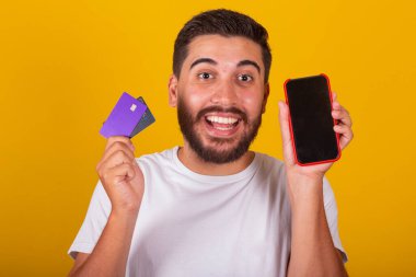 Brezilyalı Latin Amerikalı, şaşırmış ve mutlu, cep telefonu ekranı ve kredi kartı gösteriyor, cep telefonu alışverişi, uygulama, internet alışveriş konsepti.