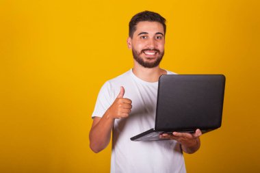 Brezilyalı Latin Amerikalı adam, mutlu, elinde not defteri ve gülümseme, başparmağıyla iş konsepti, onay, iyimserlik, teknoloji, internet erişimi.