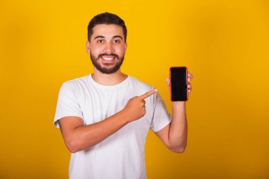 Cep telefonunu işaret eden Brezilyalı Latin Amerikalı bir adam. Uygulama, iletişim, uygulamalar, internet, 5G, sarı arka plan.