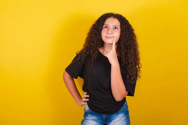 ブラジル人ラテン系アメリカ人の女の子のための アフロの髪 黄色の背景 疑いの表現 頬に指 — ストック写真