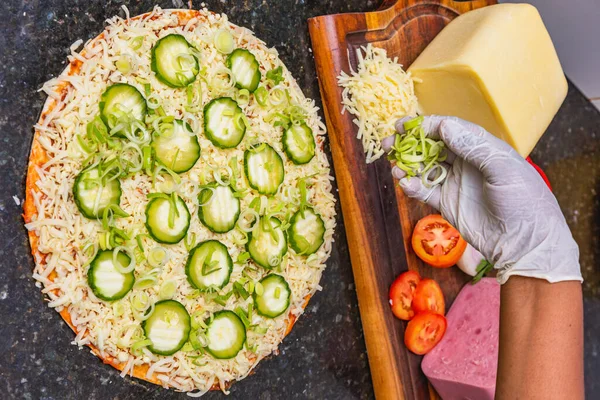 stock image Pizza preparation, spreading cucumber slices and slices on vegetarian cucumber pizza, fresh pizza ingredients on wooden board.