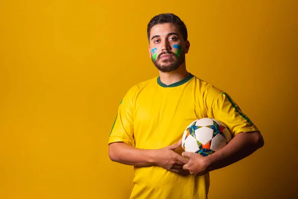 Brazilian latin american man cheering for brazil at world cup 2022, holding soccer ball, in seriousness, player, commitment, soccer cup, football. fan