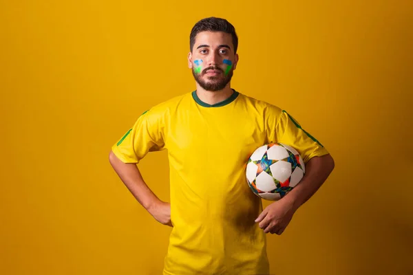 Brazilian latin american man cheering for brazil at world cup 2022, holding soccer ball, in seriousness, player, commitment, soccer cup, football. fan