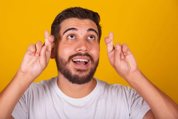 stock image Brazilian Latin American man, fingers crossed, gesture of luck, wish, hopes, cheering, lottery, yellow background.