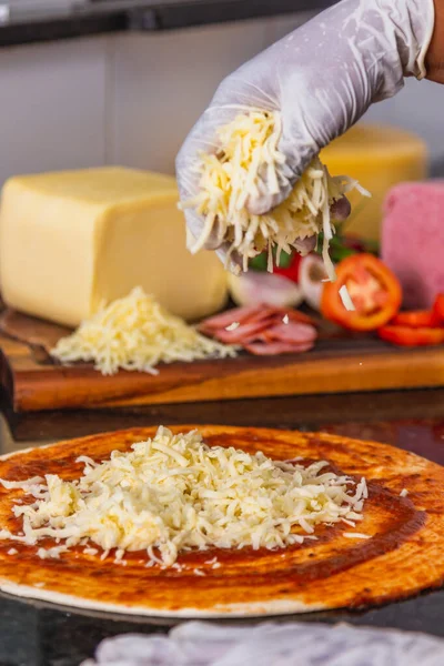 stock image Pizza preparation, spreading mozzarella cheese on pizza dough, Fresh pizza ingredients on wooden board.