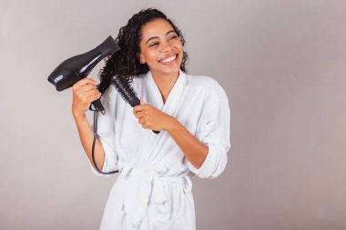 Güzel Brezilyalı siyah kadın, bornoz ve havlu giyiyor. Saç kurutma makinesi, fırça, spa, güzellik merkezi, saç bakımı..