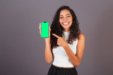 Genç Brezilyalı siyahi kadın cep telefonu tutuyor ve ekranı gösteriyor, reklam fotoğrafı..