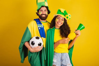 İki Brezilyalı futbol taraftarı, ulusun renginde giyinmiş, siyah kadın, beyaz erkek. bayrak ve aksesuarlar kullanarak