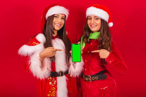 穿着圣诞服装的巴西女性朋友 圣诞老人 带绿色彩色屏幕的手机 — 图库照片