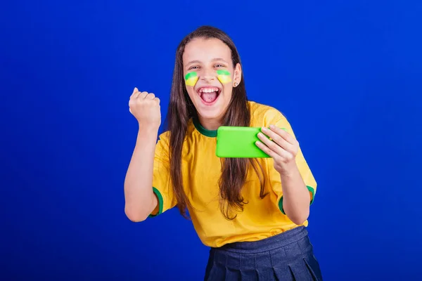 ブラジルのサッカーファンの少女です 携帯電話を持ったりゲームを見たりスマートフォンを応援したり アプリケーション — ストック写真