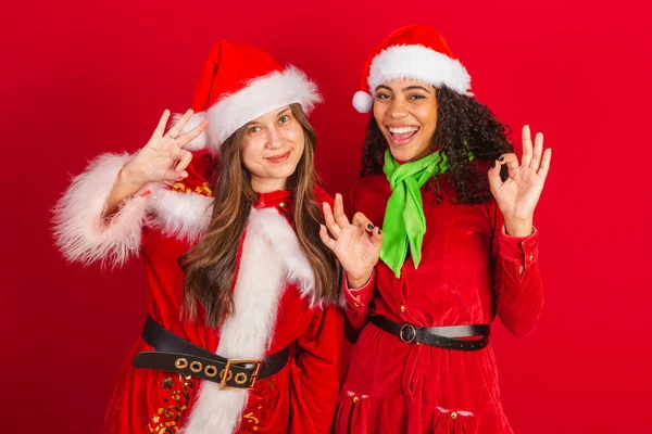 Två Brasilianska Kvinnliga Vänner Klädda Julkläder Tecken Med Fingrar — Stockfoto