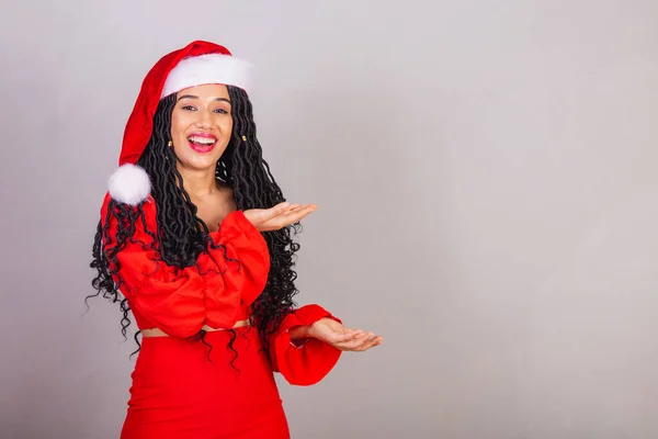 ブラジルの黒人女性はクリスマスの服を着て陽気なクリスマスに笑顔で手で何かを — ストック写真