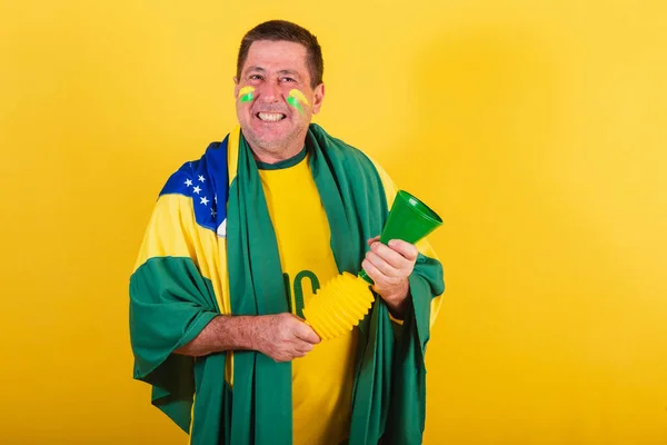 adult man, soccer fan from brazil, using flag, with horn making noise.