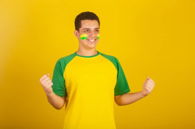 Genç Brezilyalı futbol fanatiği. Yeşil ve sarı giyinmiş, kutlama yapıyor..