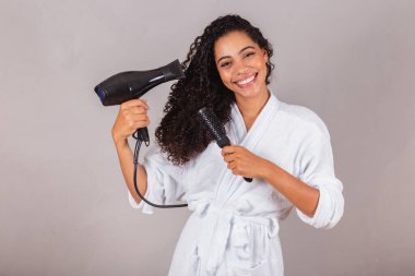 Güzel Brezilyalı siyah kadın, bornoz ve havlu giyiyor. Saç kurutma makinesi, fırça, spa, güzellik merkezi, saç bakımı..