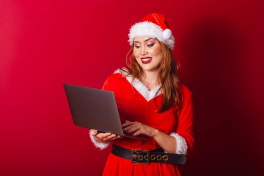 Güzel Brezilyalı kızıl saçlı kadın, Noel kıyafetleri giymiş, Noel Baba. dizüstü bilgisayarı tutuyor.