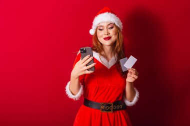 Güzel Brezilyalı kızıl saçlı kadın, Noel kıyafetleri giymiş, Noel Baba. Elinde kredi kartları ve akıllı telefon vardı..