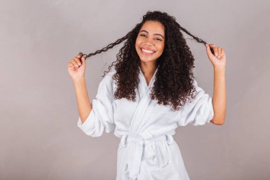 Bornoz ve havlu giymiş Brezilyalı siyahi kadın. Kıvırcık saç, spa, güzellik merkezi, saç bakımı. Saçlarını gösteriyor. bukleler.