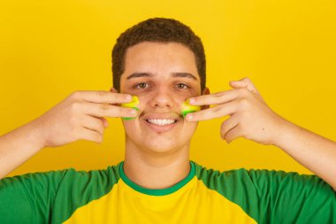Genç Brezilyalı futbol fanatiği. Yeşil ve sarı giyinmiş, yüzünü boyuyor..