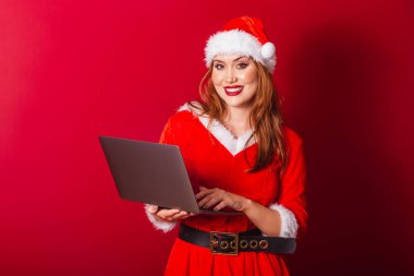 Güzel Brezilyalı kızıl saçlı kadın, Noel kıyafetleri giymiş, Noel Baba. dizüstü bilgisayarı tutuyor.