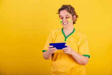 Yetişkin bir kadın, Brezilya futbol fanatiği, akıllı telefon, oyun oynuyor..