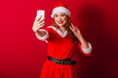 Güzel Brezilyalı kızıl saçlı kadın, Noel kıyafetleri giymiş, Noel Baba. akıllı telefondan kendi portresini çekmek.