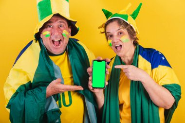 Yetişkin bir çift, Brezilya 'dan futbol taraftarı, bayrak kullanıyor. Akıllı telefon ekranına, uygulamasına, cep telefonuna, reklam fotoğrafına işaret ediyor.