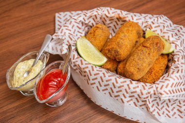 Tavuk kroket, tipik Brezilya aperatifi, limon dilimleri, acı sos ve mayonez ile servis ediliyor. Tahta masada.