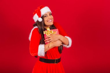Noel kıyafetleri giymiş güzel Brezilyalı kadın, Noel Baba. Kucaklayan kırmızı hediye.