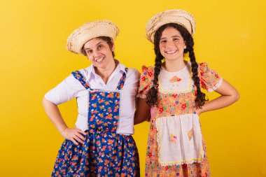 Büyükanne ve torun tipik Festa Junina kıyafetleri giymişler. Eller kalçada, gülümsüyor..