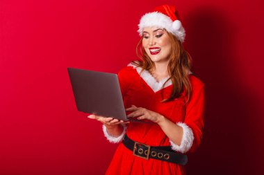 Güzel Brezilyalı kızıl saçlı kadın, Noel kıyafetleri giymiş, Noel Baba. dizüstü bilgisayarı tutuyor.