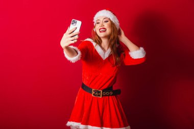 Güzel Brezilyalı kızıl saçlı kadın, Noel kıyafetleri giymiş, Noel Baba. akıllı telefondan kendi portresini çekmek.