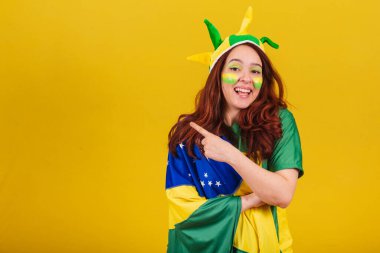 Kafkasyalı, kızıl saçlı, Brezilyalı futbol taraftarı, işaret parmağıyla solu işaret ediyor. Reklam fotoğrafı.