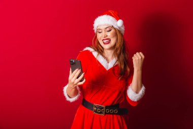Güzel Brezilyalı kızıl saçlı kadın, Noel kıyafetleri giymiş, Noel Baba. Akıllı telefonla kutlama.