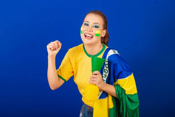白人妇女 红头发 巴西足球迷 巴西人 蓝色背景 手持旗帜和号角跳舞 — 图库照片