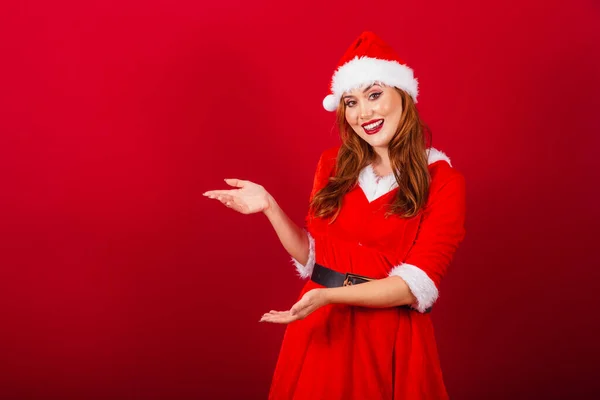 美しいブラジルの赤髪の女性 クリスマス服を着て サンタクロース 左側に何かを — ストック写真