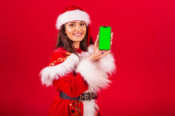 穿圣诞服装的巴西女人圣诞老人手持带有绿色屏幕的彩色智能手机 — 图库照片